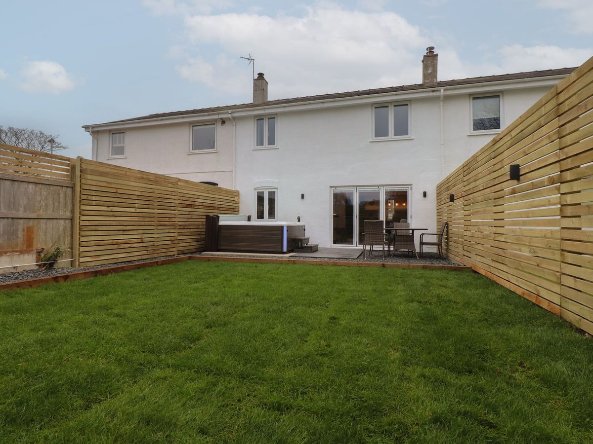 Sea Cliff rear lawn with slatted timber fencing, a hot tub and a patio table and chairs by the white house