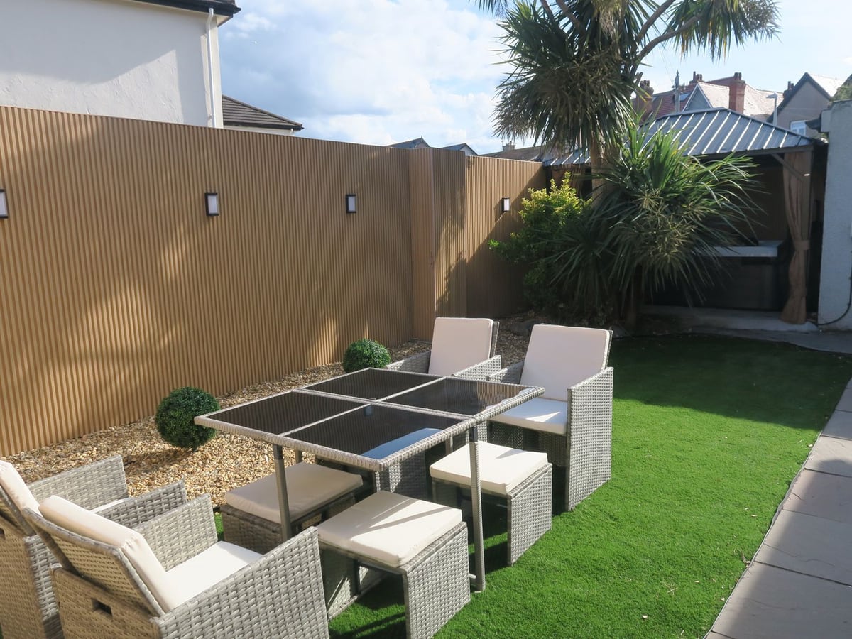 Seabreeze rear garden with artificial grass, rattan dining set, tall fence and hot tub under a gazebo