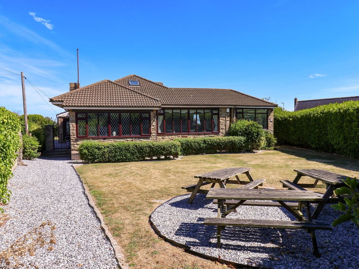 Seacrest Lodge exterior with a lawn, gravel path and wooden picnic tables beside hedges