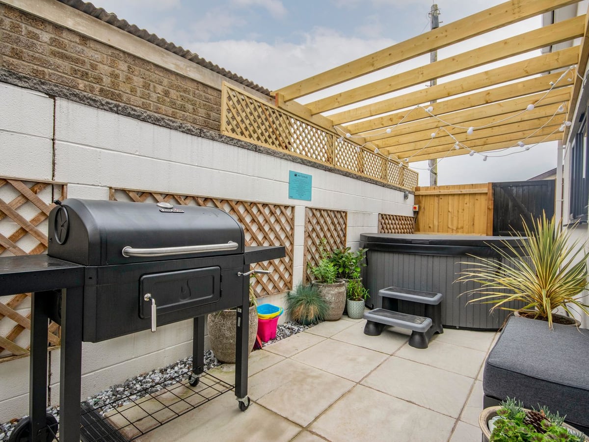 Seagull Shack walled rear patio with a hot tub with its lid on, open pergola, barbecue and plants