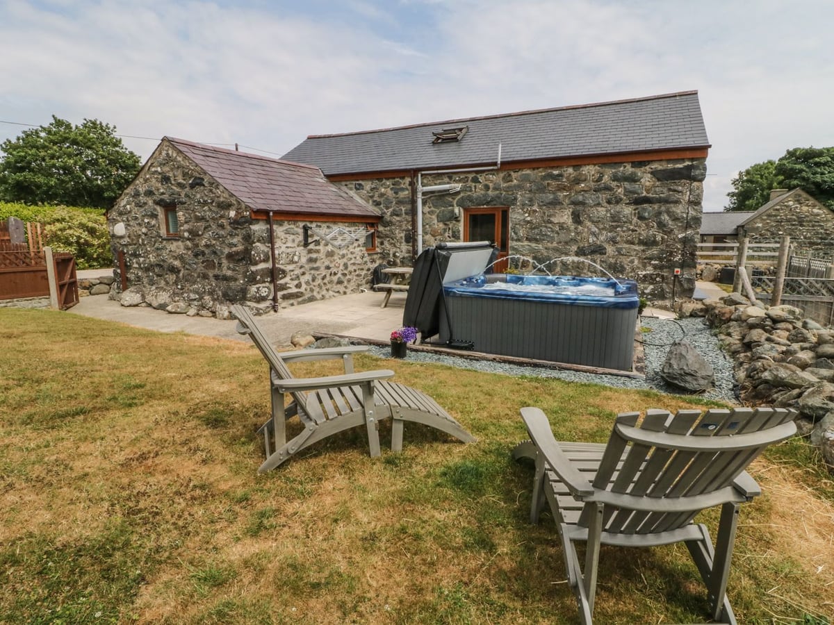 Sgubor stone barn with a hot tub on gravel and two wooden loungers on the lawn in front