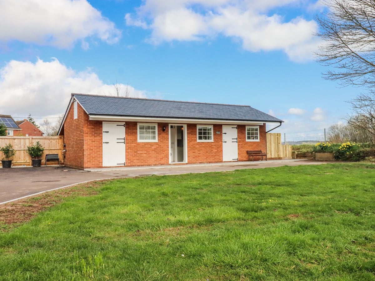 Single-storey red-brick Shamrock cottage with white doors and a lawn in front