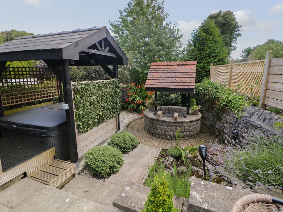 Shenton Cottage garden with a paved path, planted borders, stone well and covered hot tub