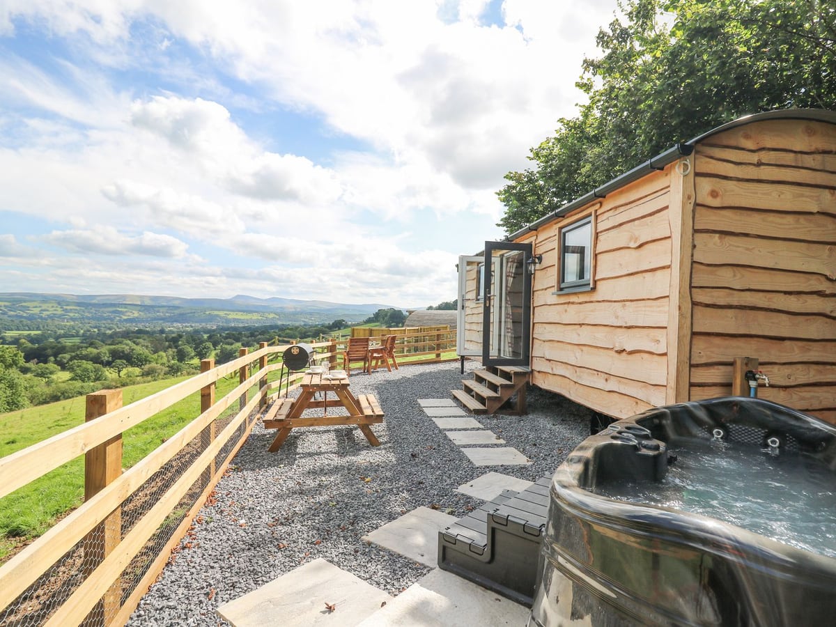 Hot tub, gravel seating area and picnic bench beside Shepherd's Cwtch hut, with fenced valley view
