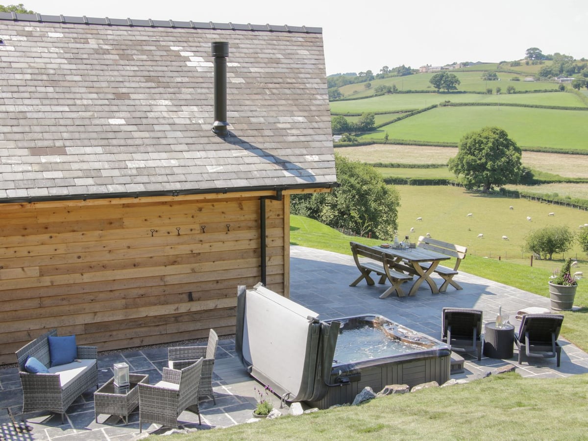 Shepherd's Rest slate patio with an open hot tub, wicker seats and picnic table beside a lawn and fields