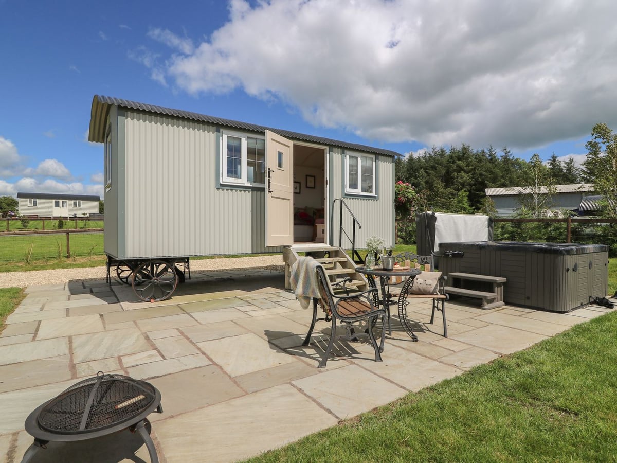 Shepherd's View hut on wheels with a stone patio, bistro set, fire pit and hot tub beside a lawn