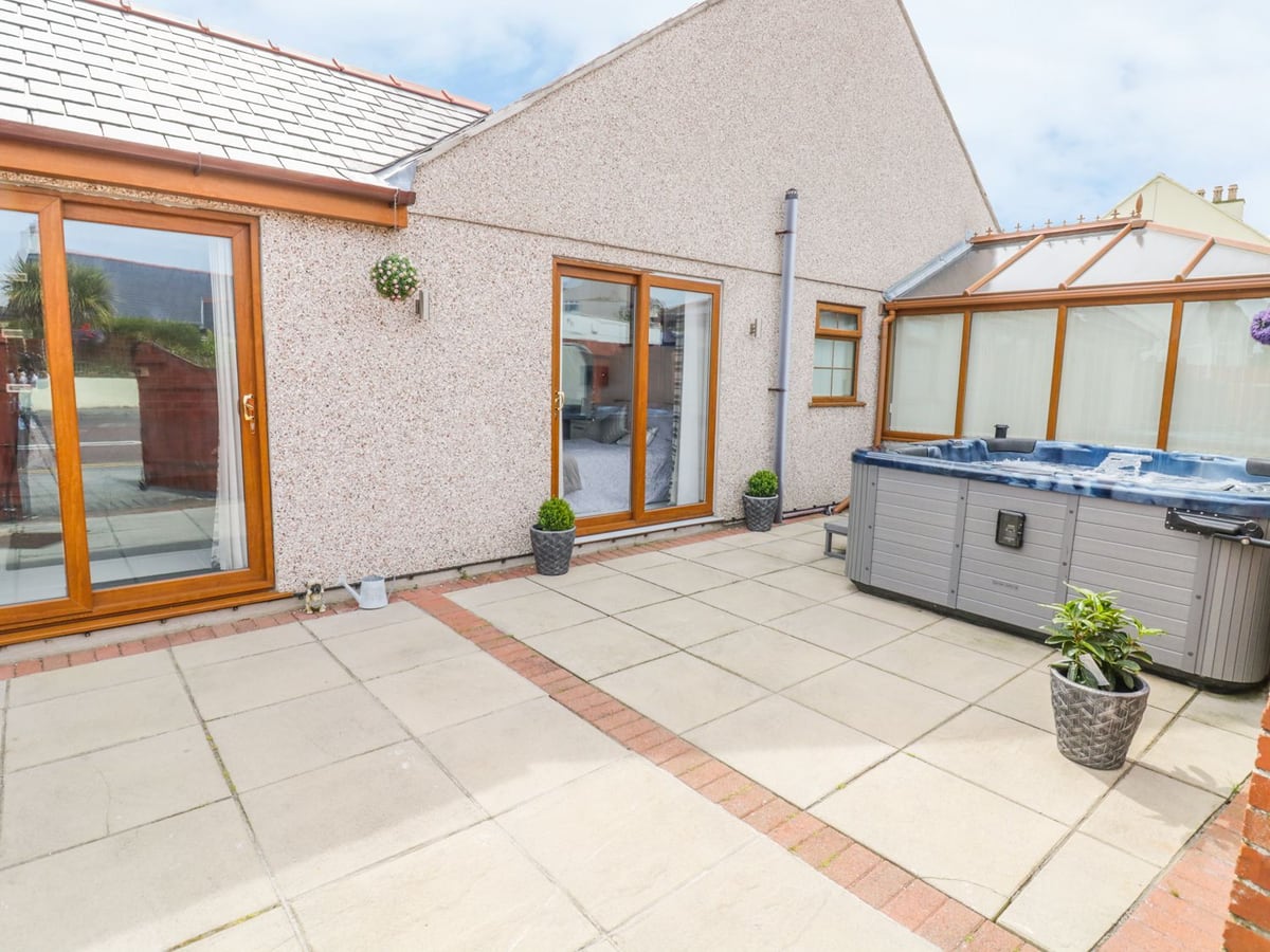 Smithy Cottage paved patio with an open hot tub, two sets of patio doors, potted plants and a conservatory
