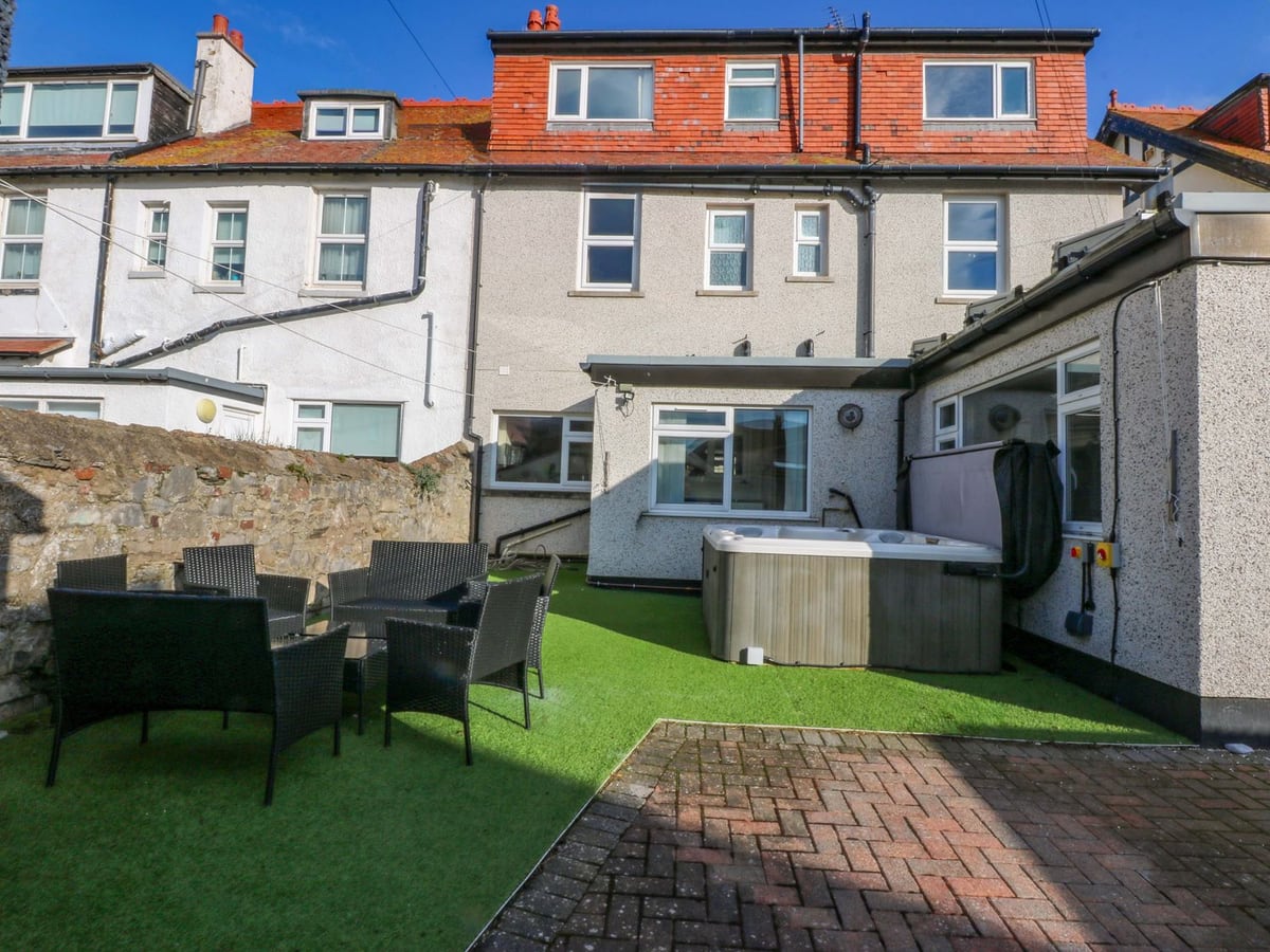 Southbourne Manor rear garden with artificial lawn, rattan-style seating, hot tub and brick paving