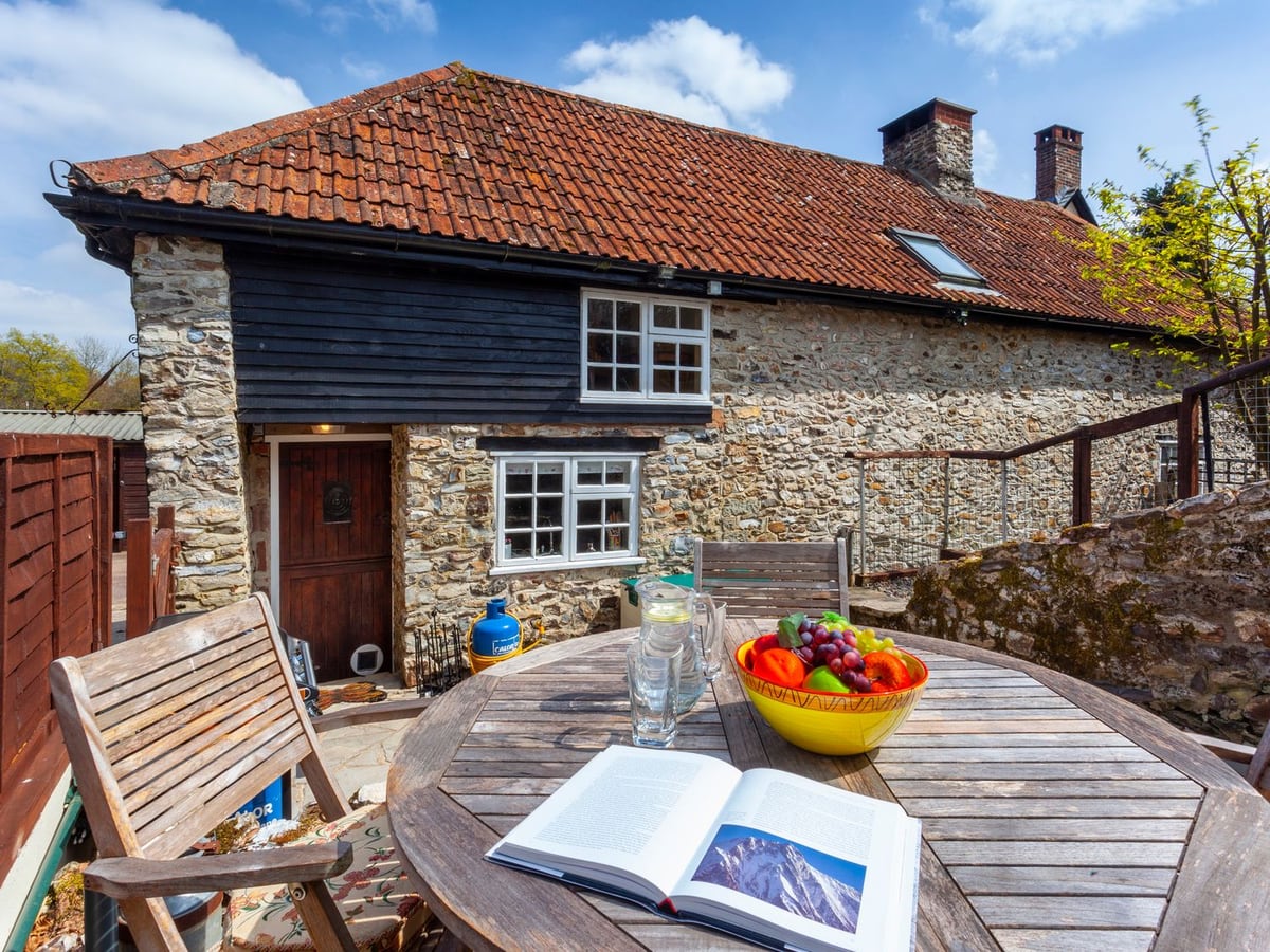Stone cottage with red roof tiles above a terraced dining area at Southcott Farm Cottage