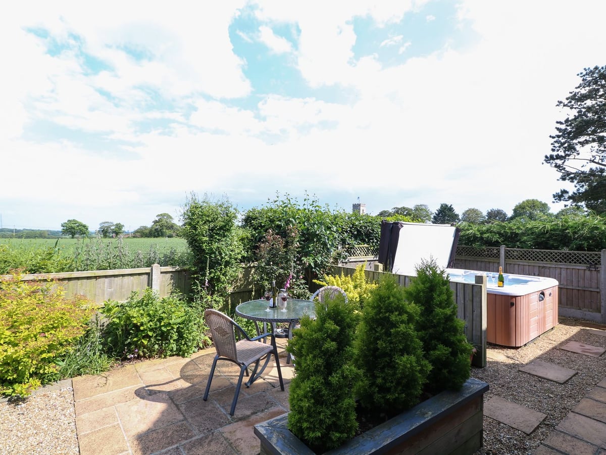 Small patio with a table, chairs and hot tub beside planted borders at Spinney's Den