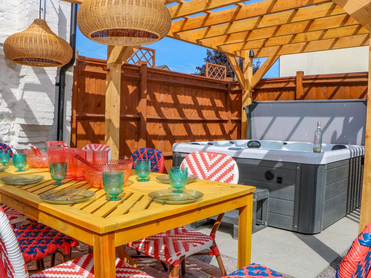 Hot tub and colourful dining chairs beneath a wooden pergola beside Spring Cottage