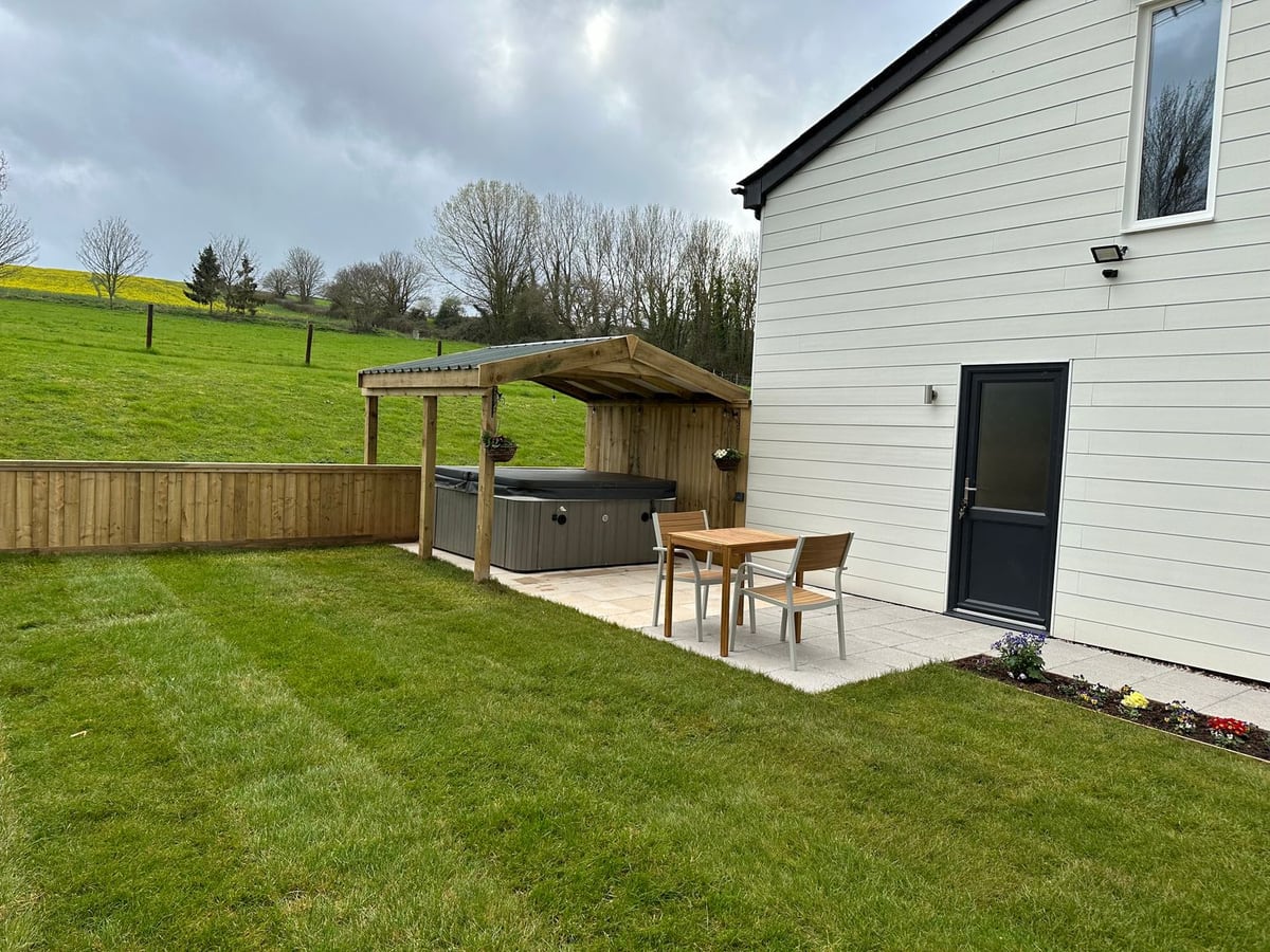 White cladding, lawn and a hot tub beneath a timber shelter at Springwell Lodge