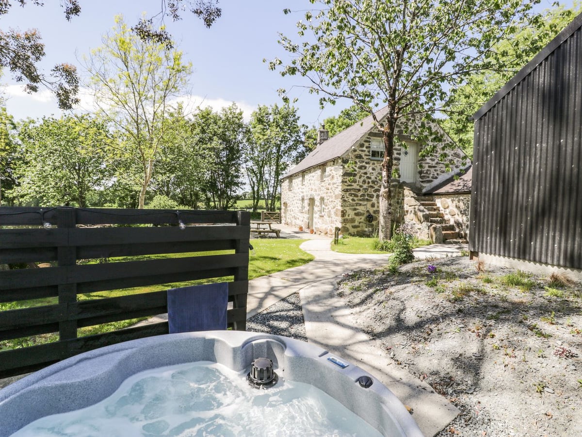 Hot tub beside a wooden screen, with lawn, paths, picnic bench and Stabla's stone cottage beyond