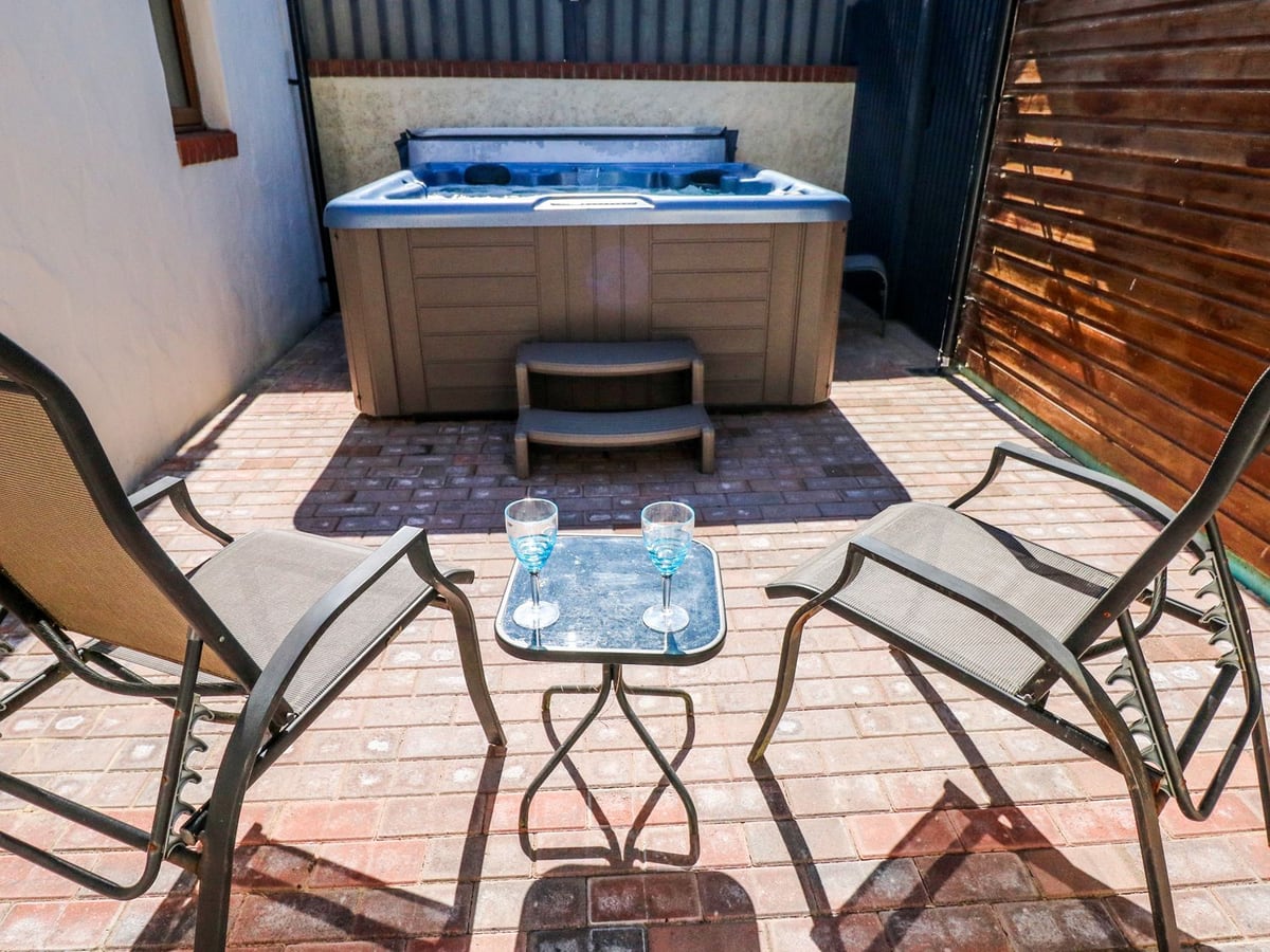 Stable Cottage brick-paved courtyard with two reclining chairs, a small table and hot tub at the far end
