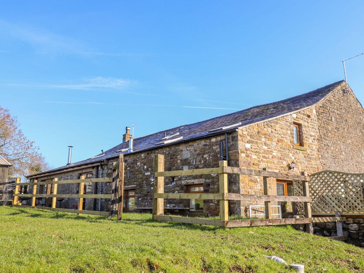 Stone exterior of Stable View Cottage beside timber fencing and a grassy bank