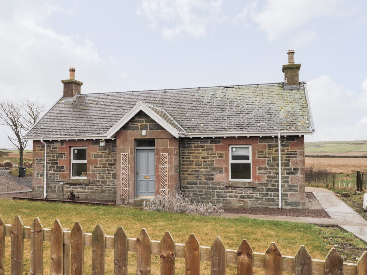 Station House stone cottage with a picket fence, front lawn and open farmland beyond