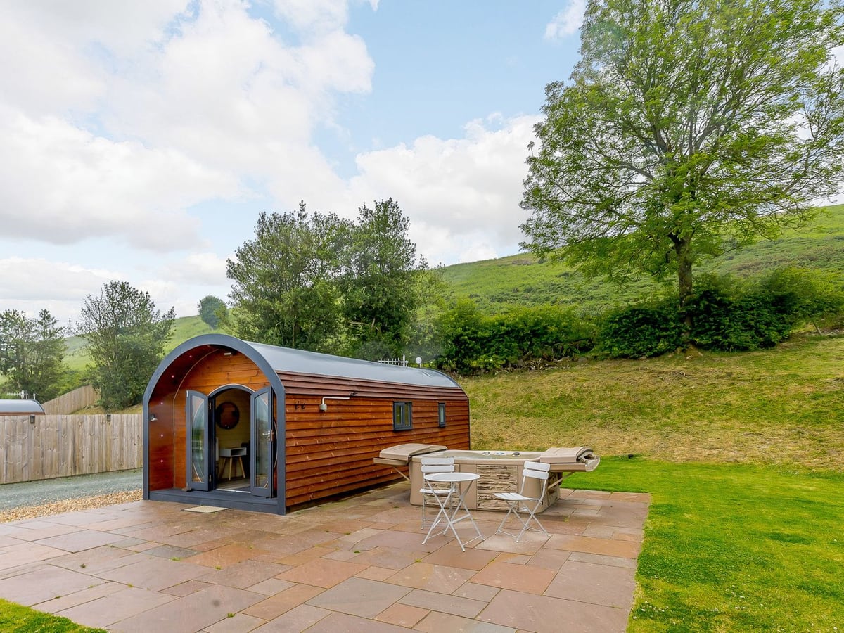 Stiperstones Pod beside its hot tub, paved terrace and lawn beneath the hillside