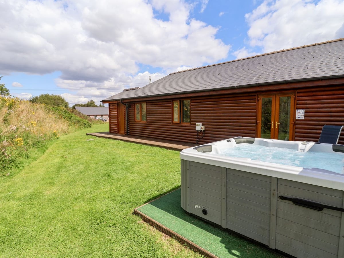 Hot tub beside Sunset Lodge No.6 with lawn running along its timber exterior