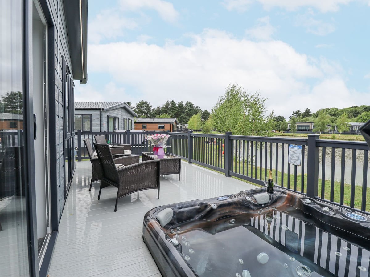 Hot tub and wicker seating on Sunset Lodge's lakeside deck in Woodhall Spa