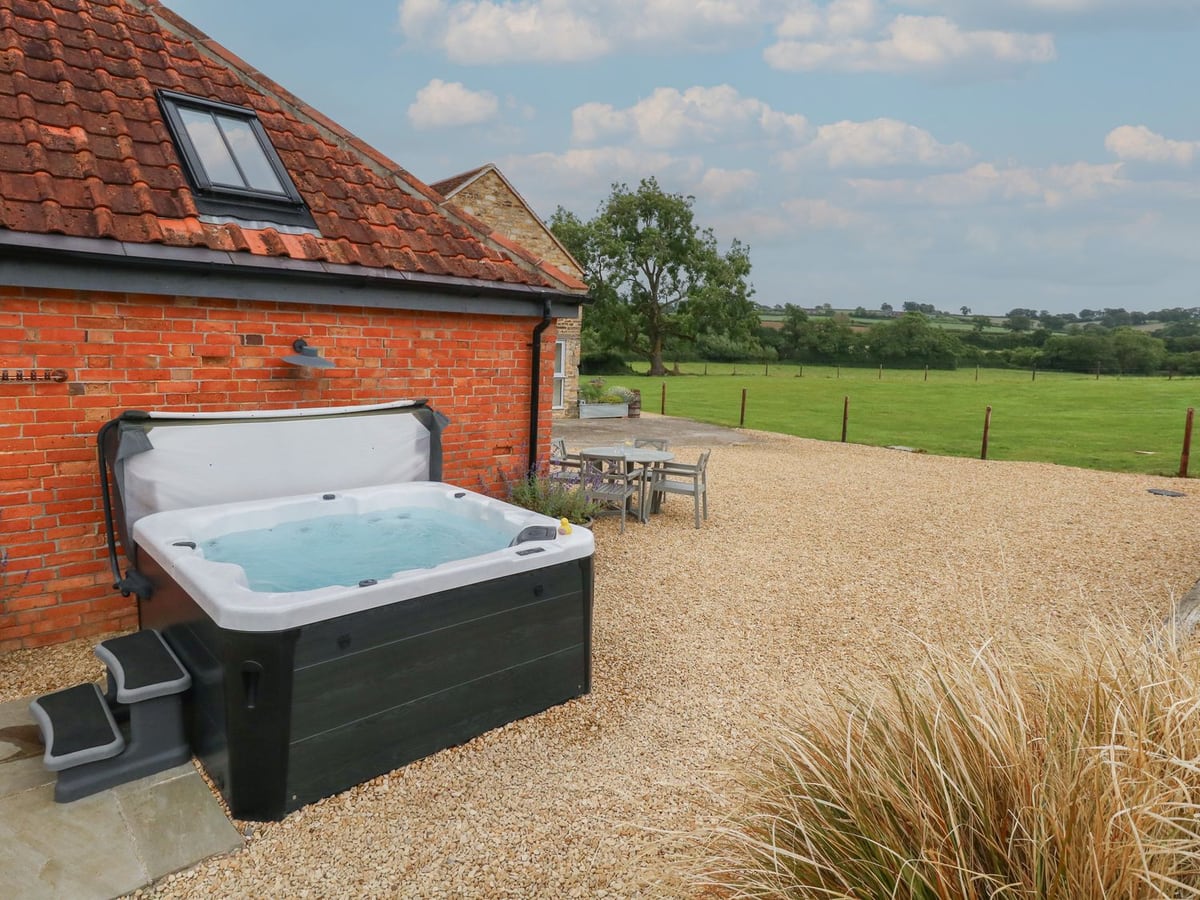 Hot tub against the brick wall of Swallows Nest, with gravel seating space and fields beyond
