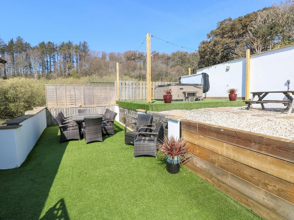 Swn y mor garden with artificial lawn, rattan dining set and a hot tub on a raised terrace