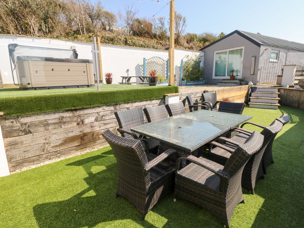 Swn y mor terrace with outdoor dining, a raised hot tub area and a grey garden building