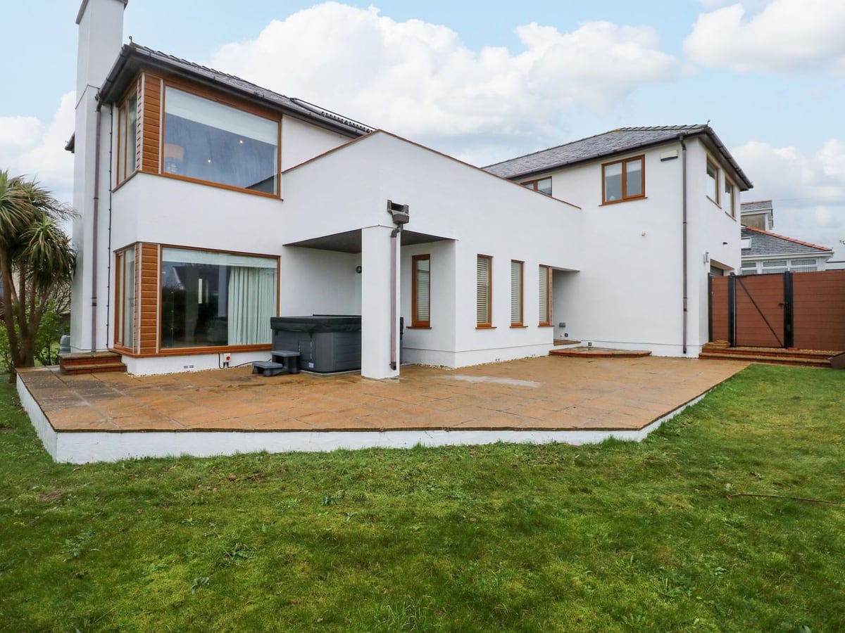 Swyn Y Llyr rear exterior with broad patio, lawn and a covered hot tub beside the house