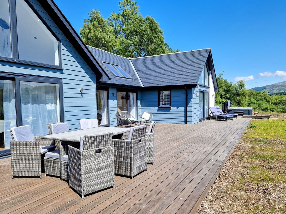 Taigh Moy blue-clad exterior with a broad timber deck, outdoor dining seats and loungers