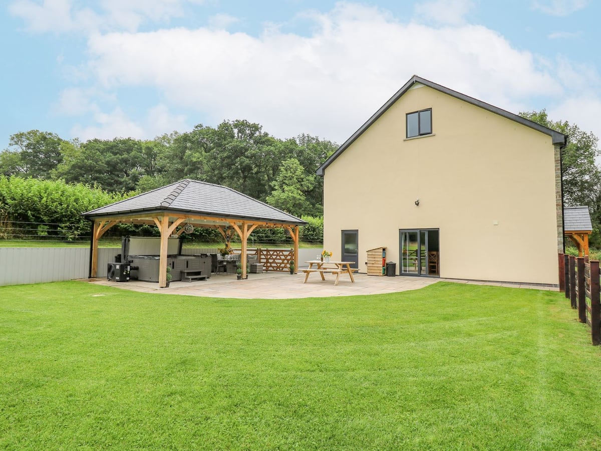 Talarddu Cottage rear lawn and patio with a picnic bench and a timber pavilion covering a hot tub