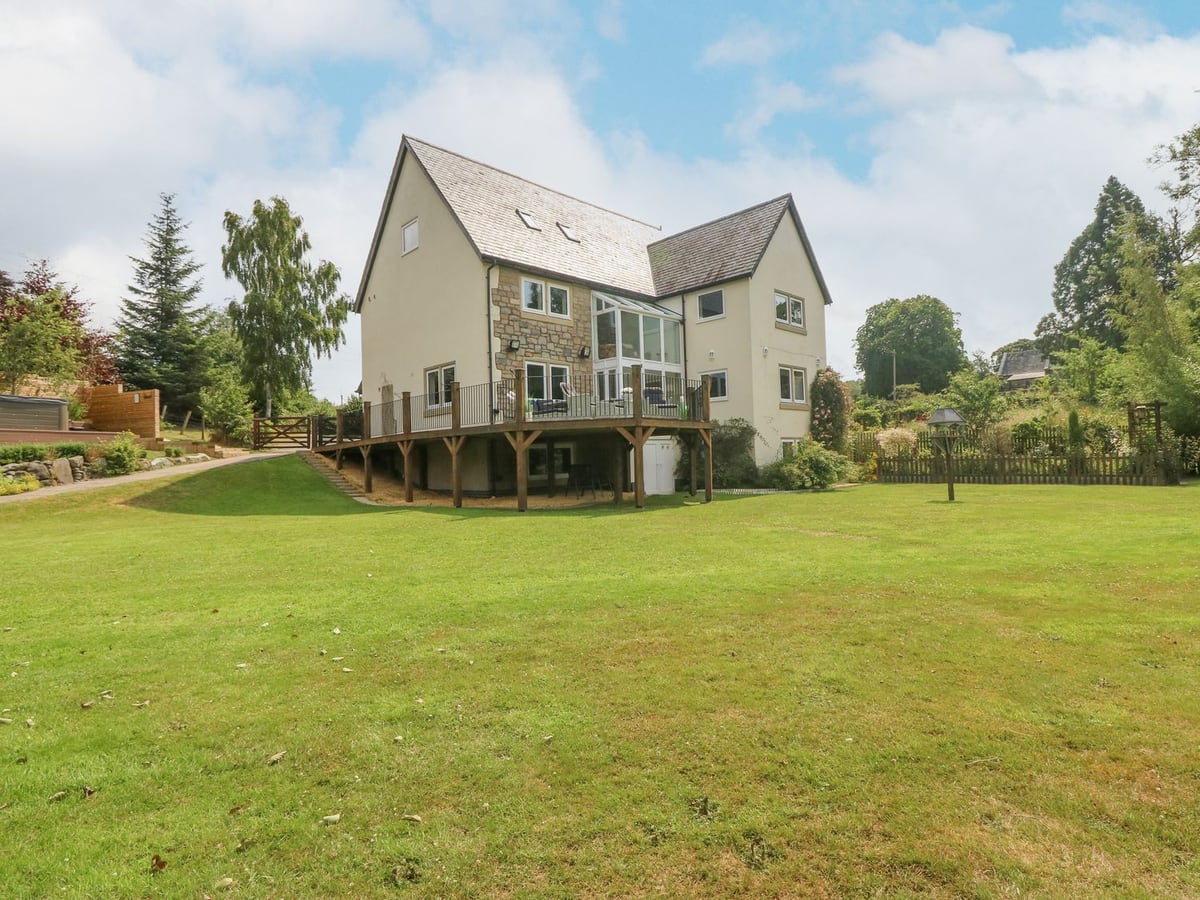 Tan Yr Allt, a large rendered and stone house with a raised timber deck overlooking a wide mown lawn