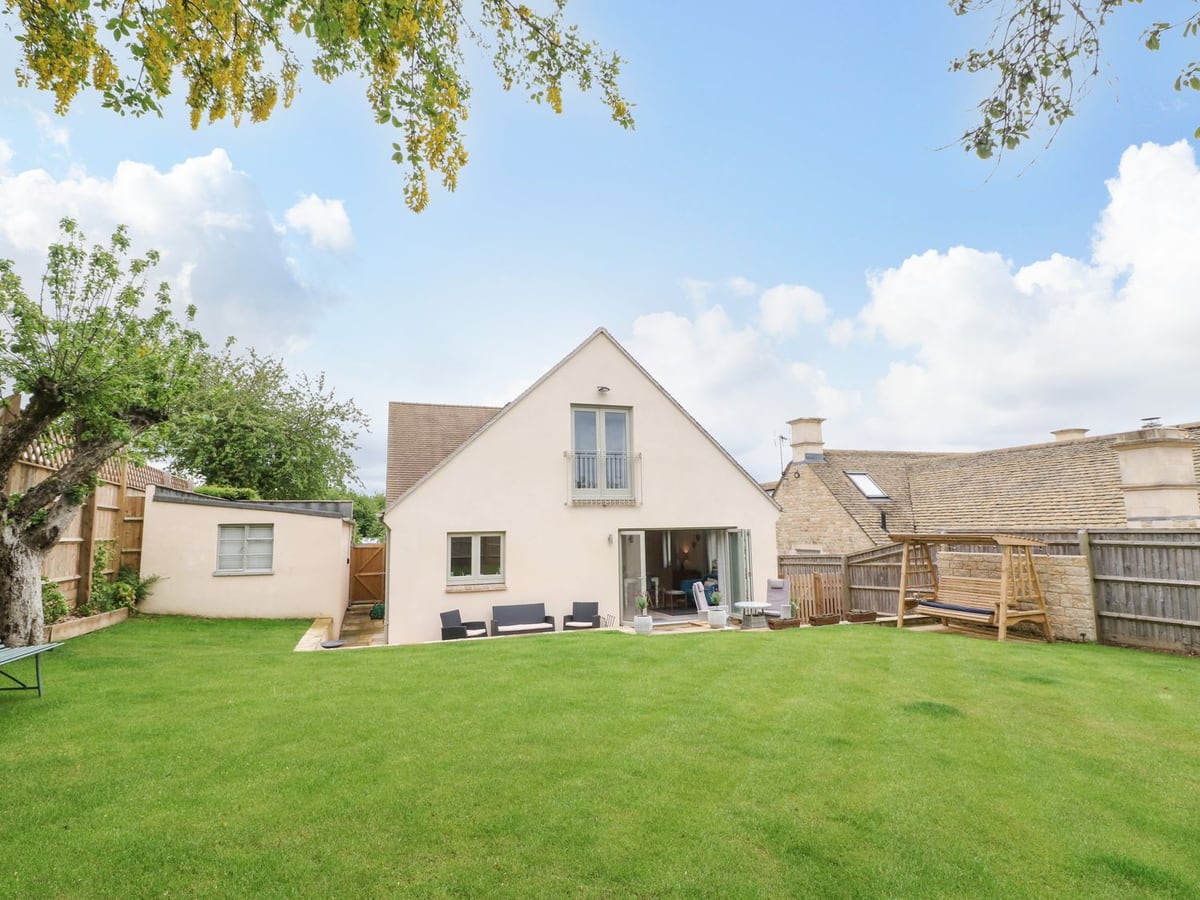 Tawny Cottage facing a broad green lawn with outdoor chairs, a swing seat and timber fencing