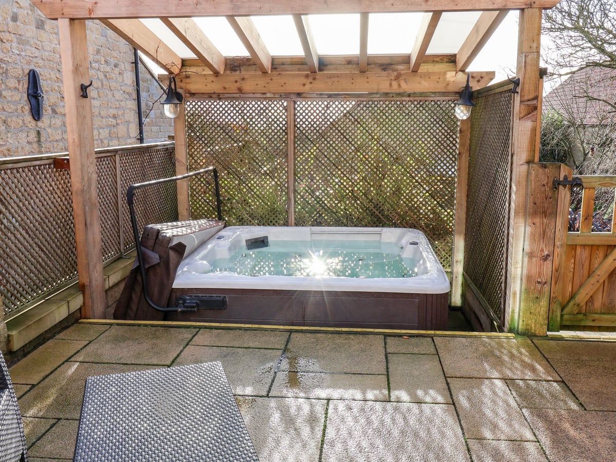 Hot tub under a timber pergola on the stone patio at Tawny Cottage near Scarborough