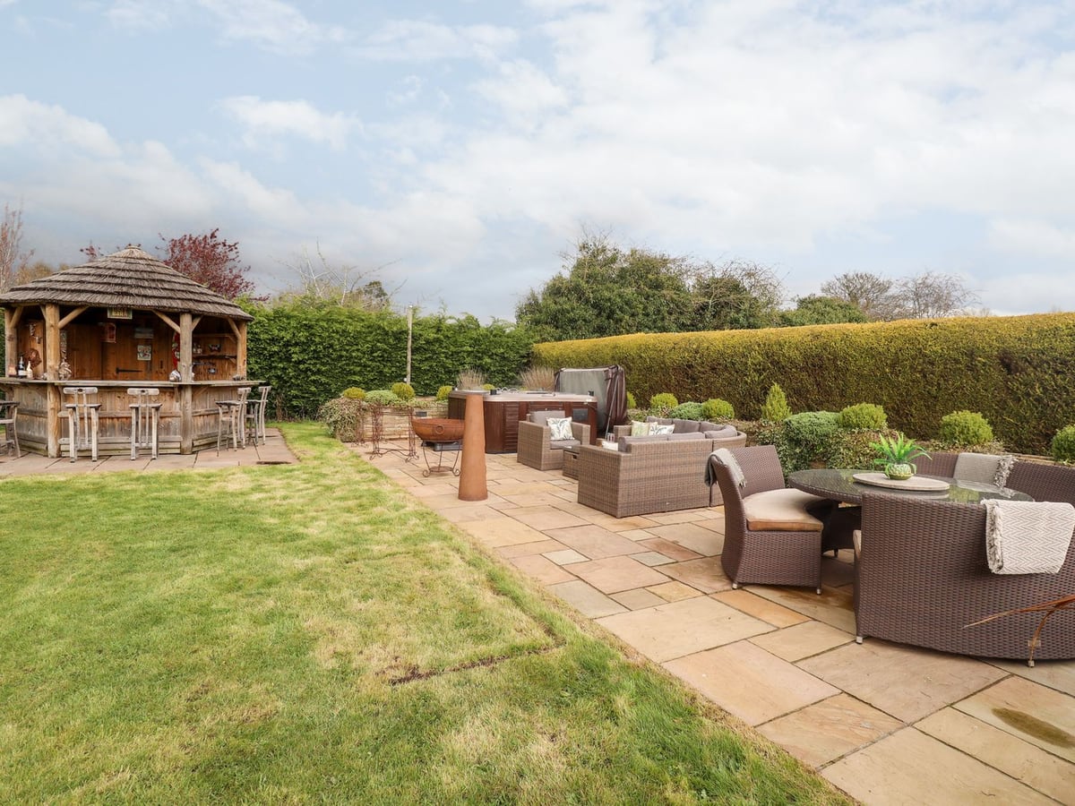 Lawn, patio seating, timber bar and hot tub at Tawny Owl Cottage
