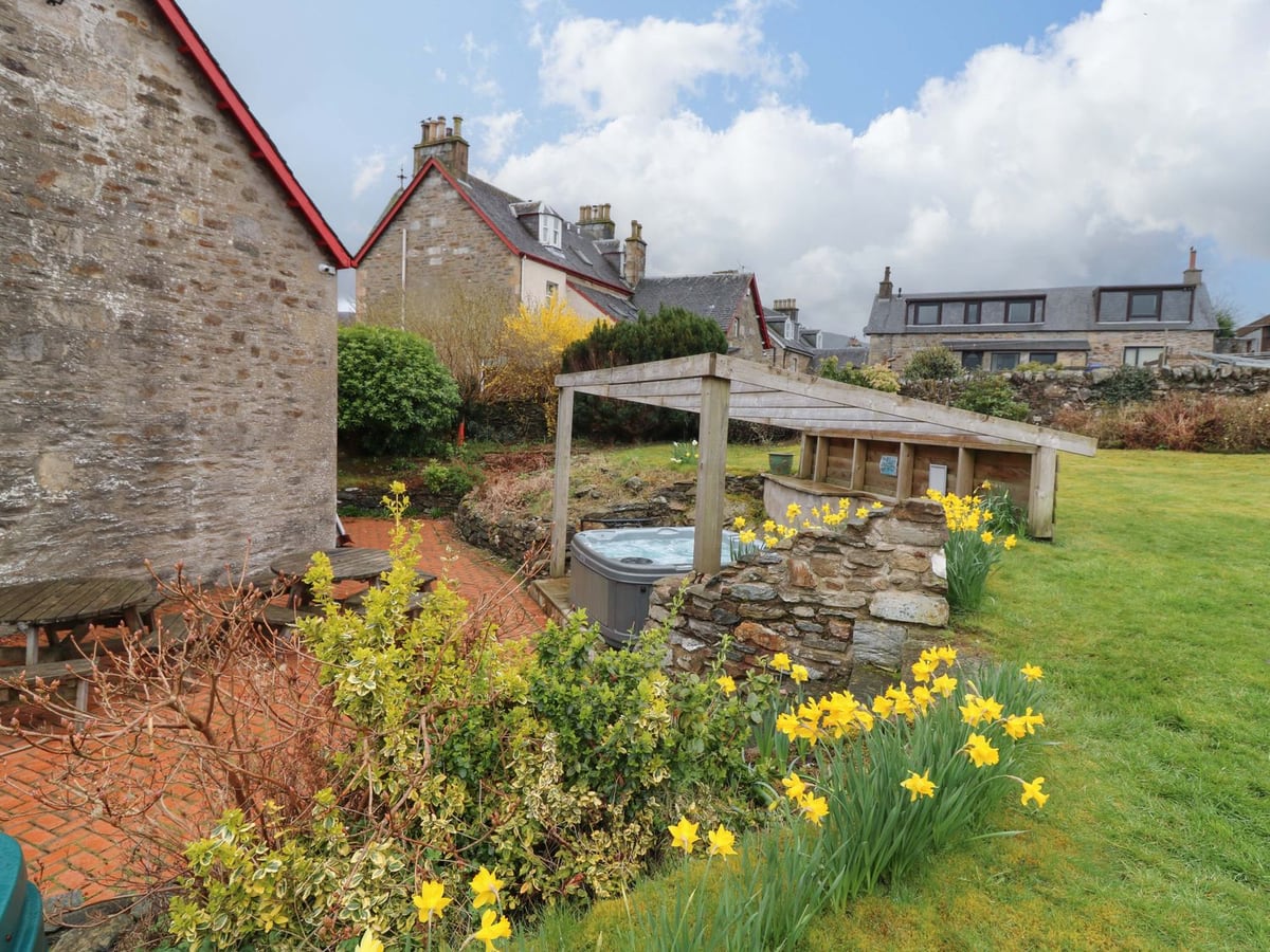 Tayview garden with a lawn, daffodils and a sheltered hot tub beside the stone house