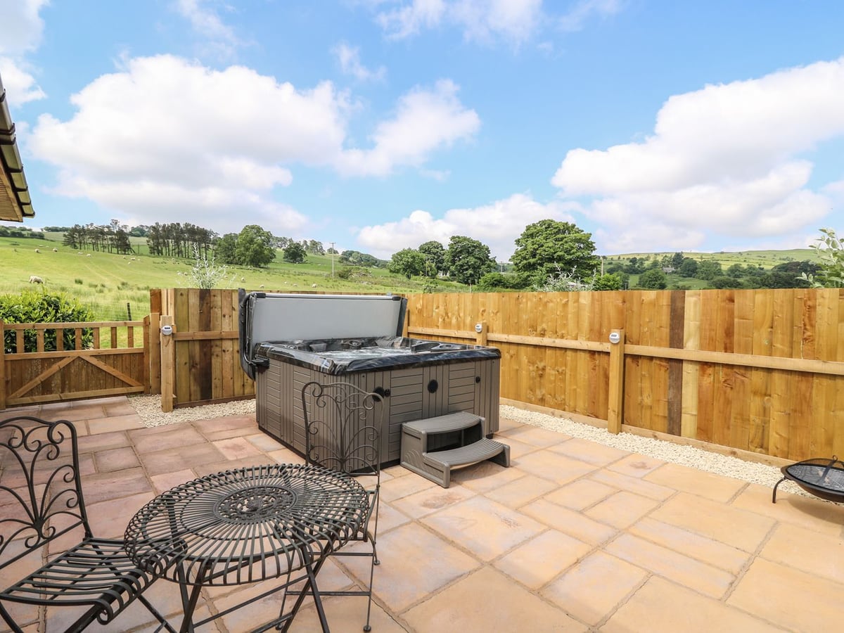 Tegfan paved patio with hot tub, iron table and chairs, wooden fencing and fields beyond