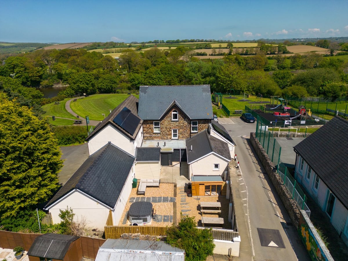Aerial view of Teifi Villa with a fenced gravel courtyard, covered hot tub, picnic tables and lawns beyond
