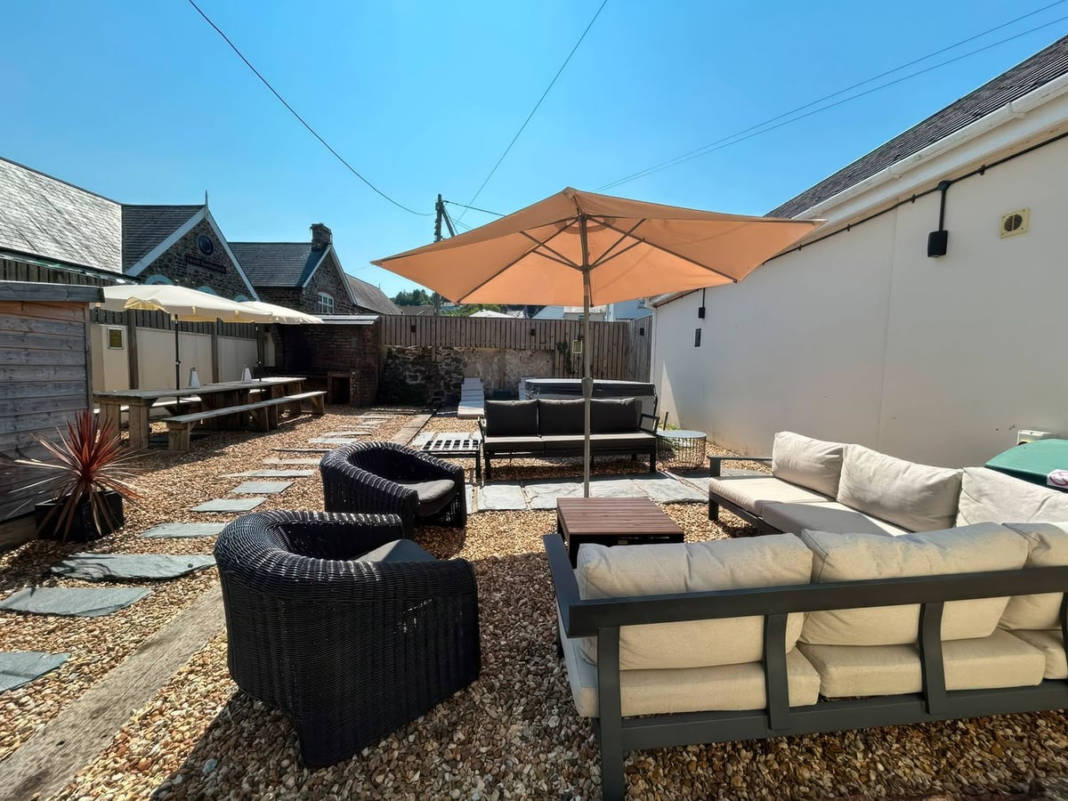 Gravel courtyard with outdoor sofas, dining tables and parasols at Teifi Villa