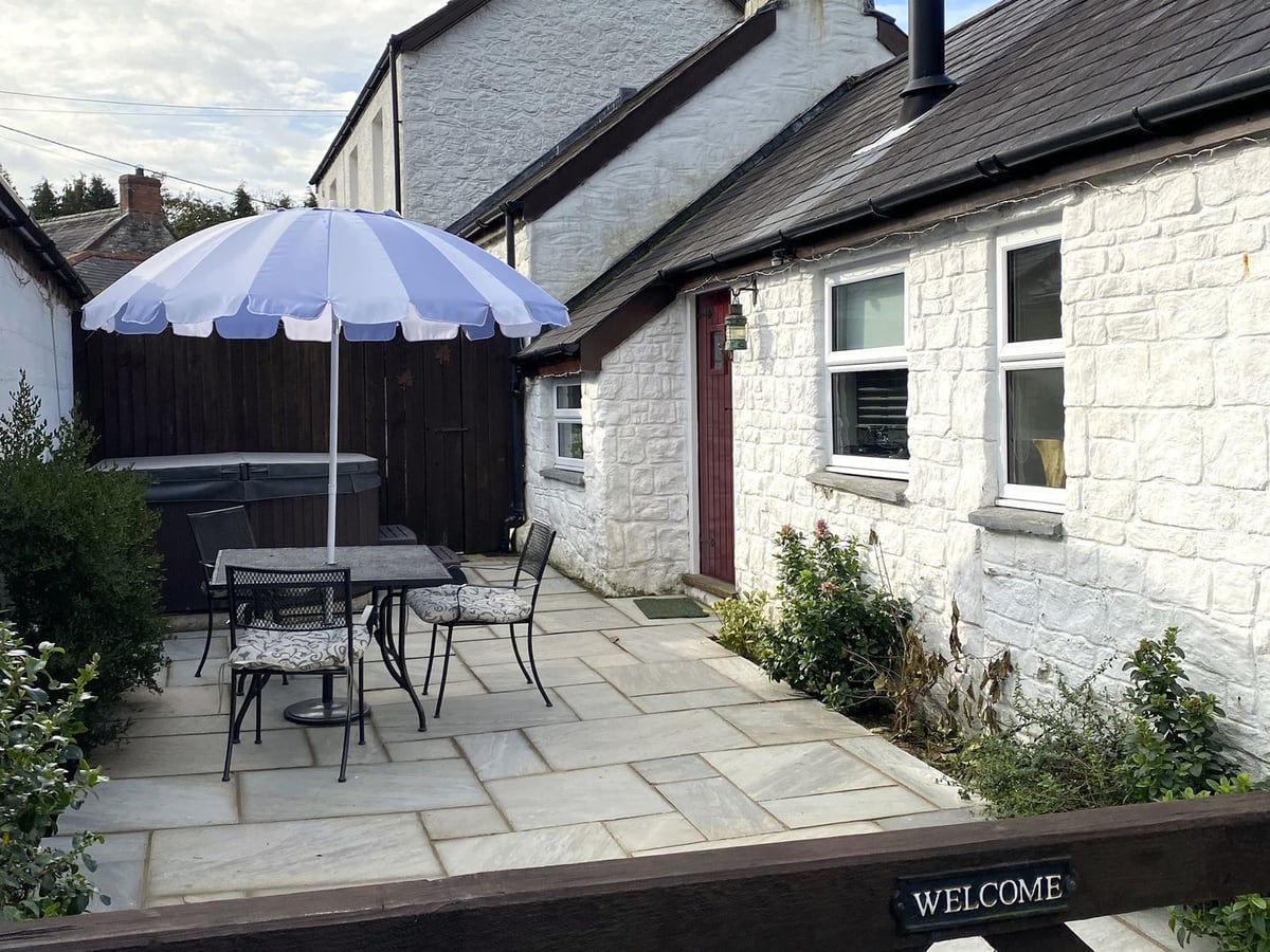 The Barn at Waunlippa courtyard with parasol table, hot tub with its lid on and whitewashed stone walls