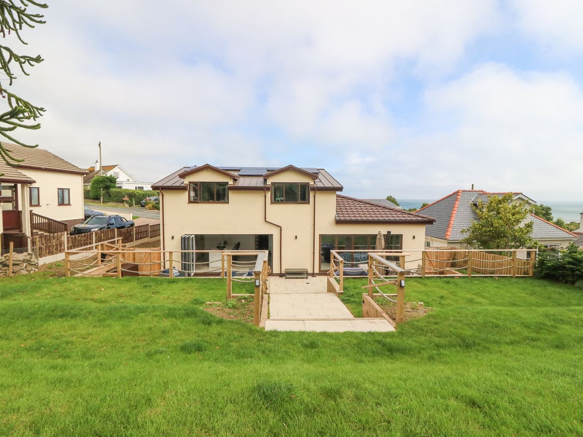 The Bay rear view with a sloping lawn, paved steps, rope-railed patio and a sea glimpse beyond