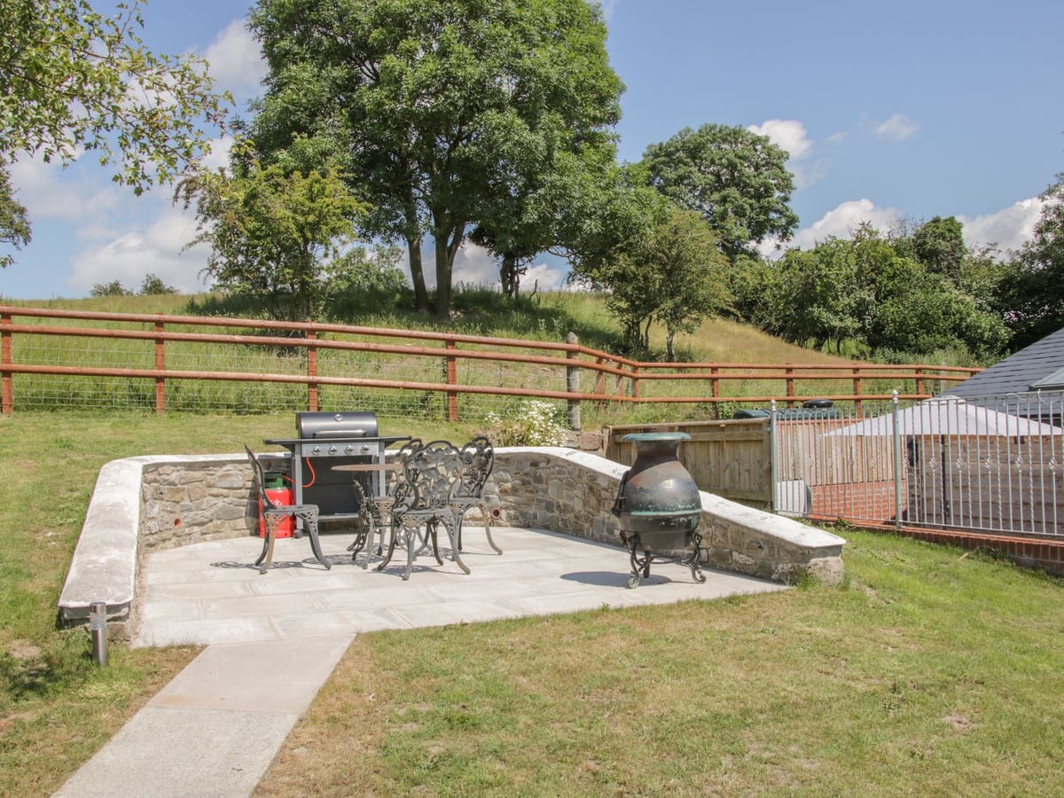 Stone seating terrace, barbecue and lawn above The Boundary Annex, with fencing behind