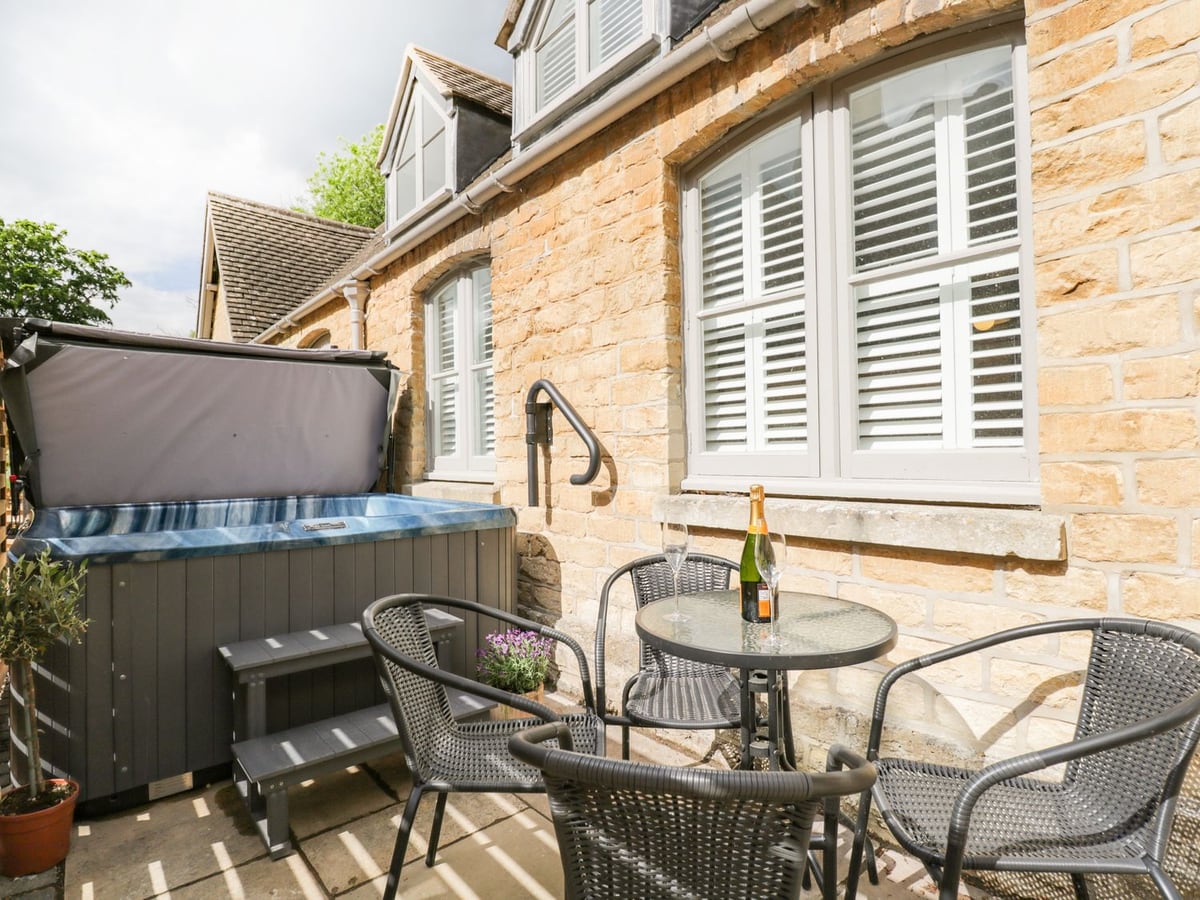 The Coach House hot tub beside its stone wall, with a round glass table and outdoor chairs