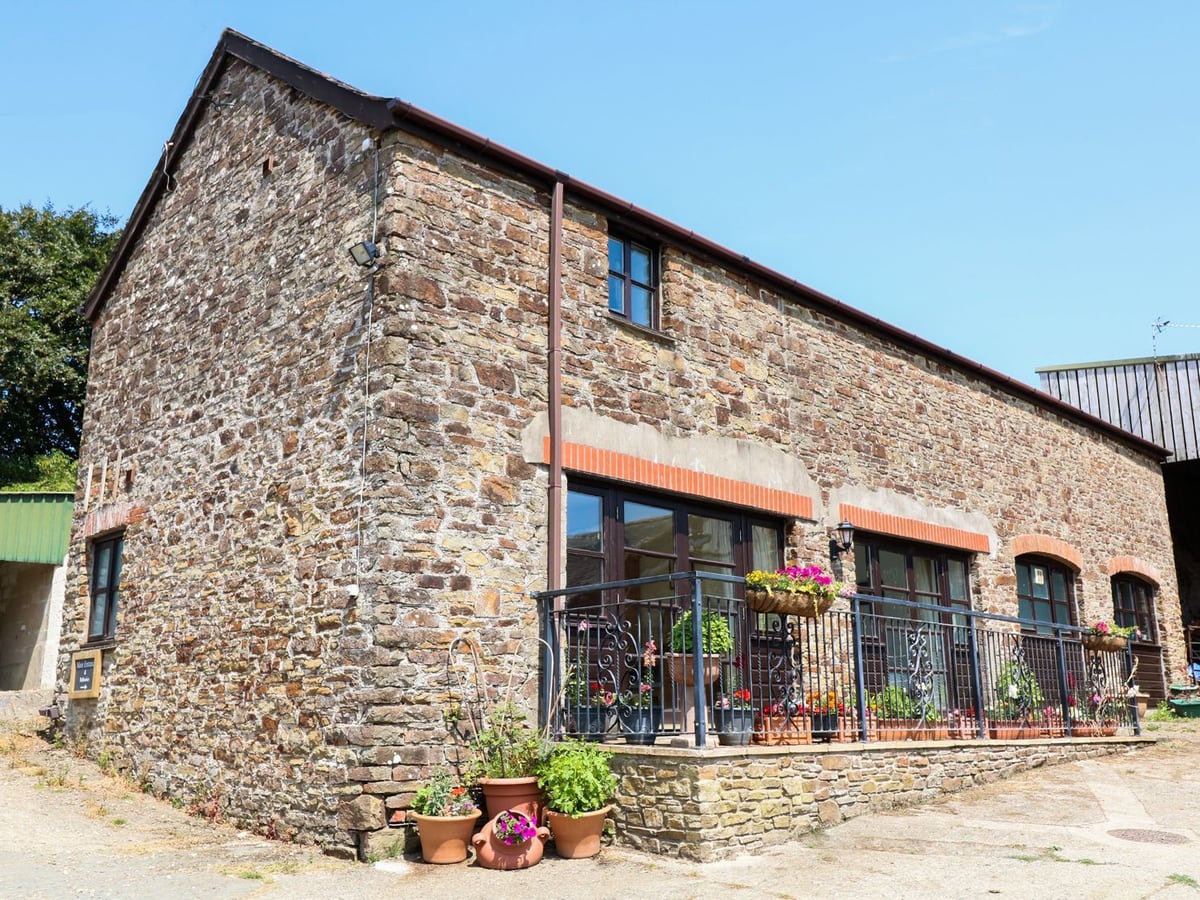 Stone barn facade with glazed doors, iron railings and flower pots at The Corn Tallet