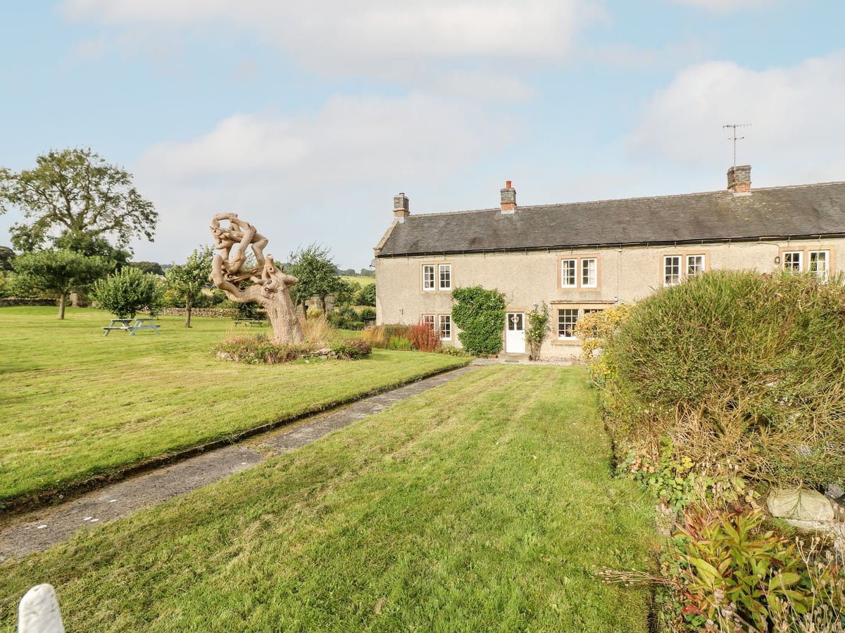 The Farmhouse with a broad lawn, stone path, shrubs and picnic tables beside the house
