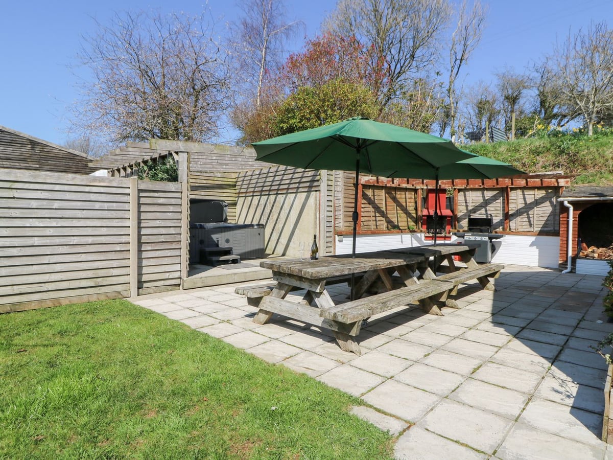 The Farmhouse patio with picnic tables, green parasols, a lawn edge and a hot tub with its lid on