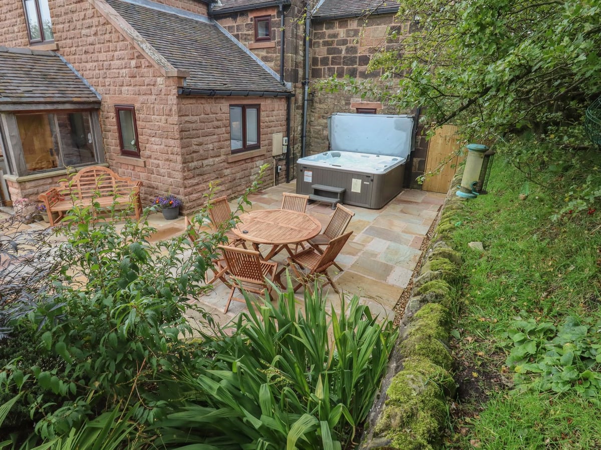 Hot tub and wooden dining table on the stone patio beside The Farmhouse at Biddulph Moor.