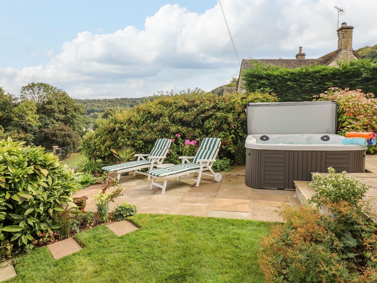 Hot tub and striped loungers beside a lawn and planted borders in the garden at The Gables