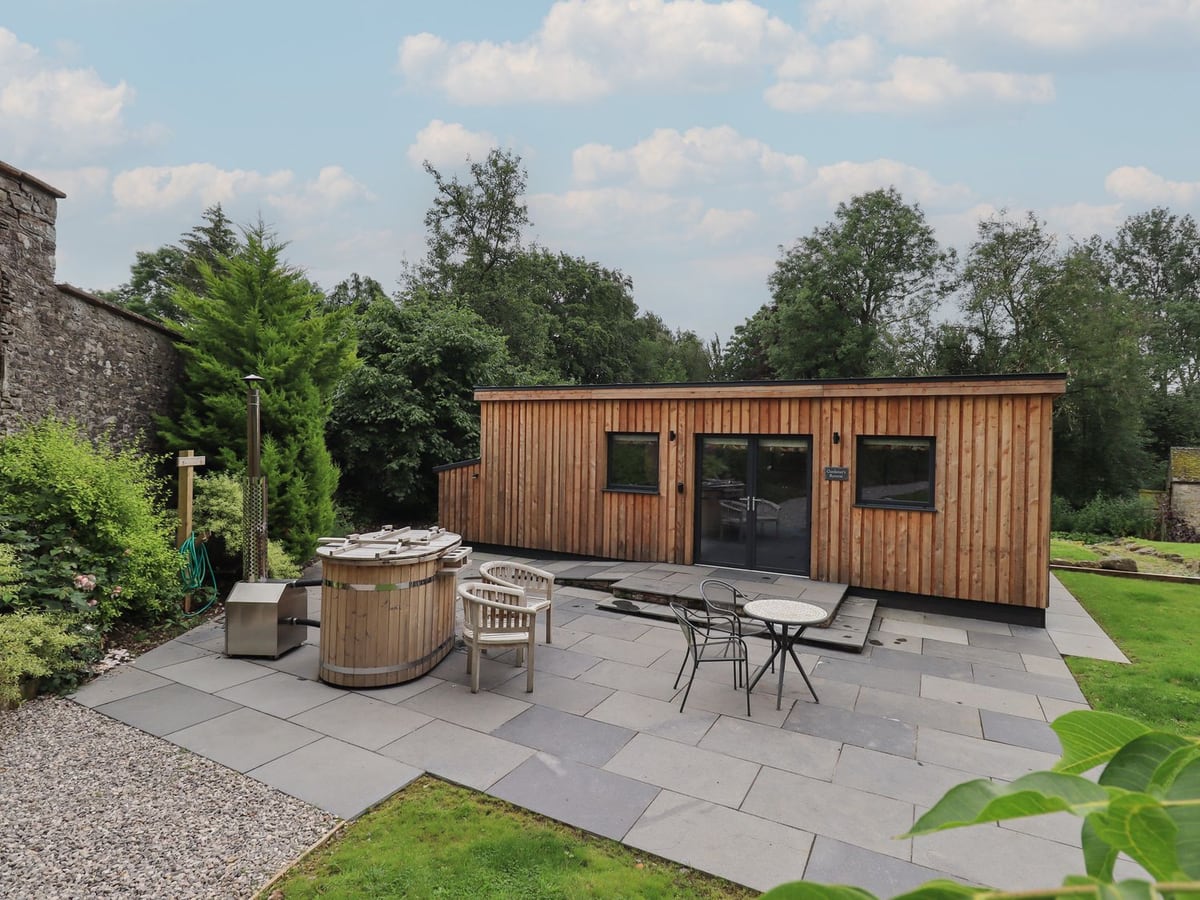 The Gardener's Retreat timber cabin beside a round wooden hot tub and paved seating area