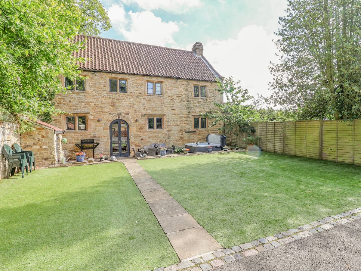 The Gatehouse stone exterior with a lawn, garden fence and hot tub beside the house