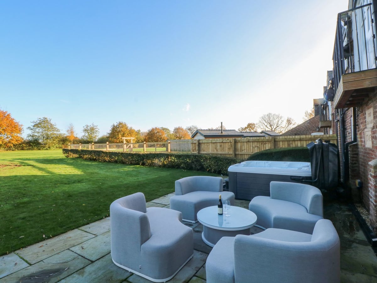 Hot tub, patio chairs and lawn beside the red-brick exterior of The Granary