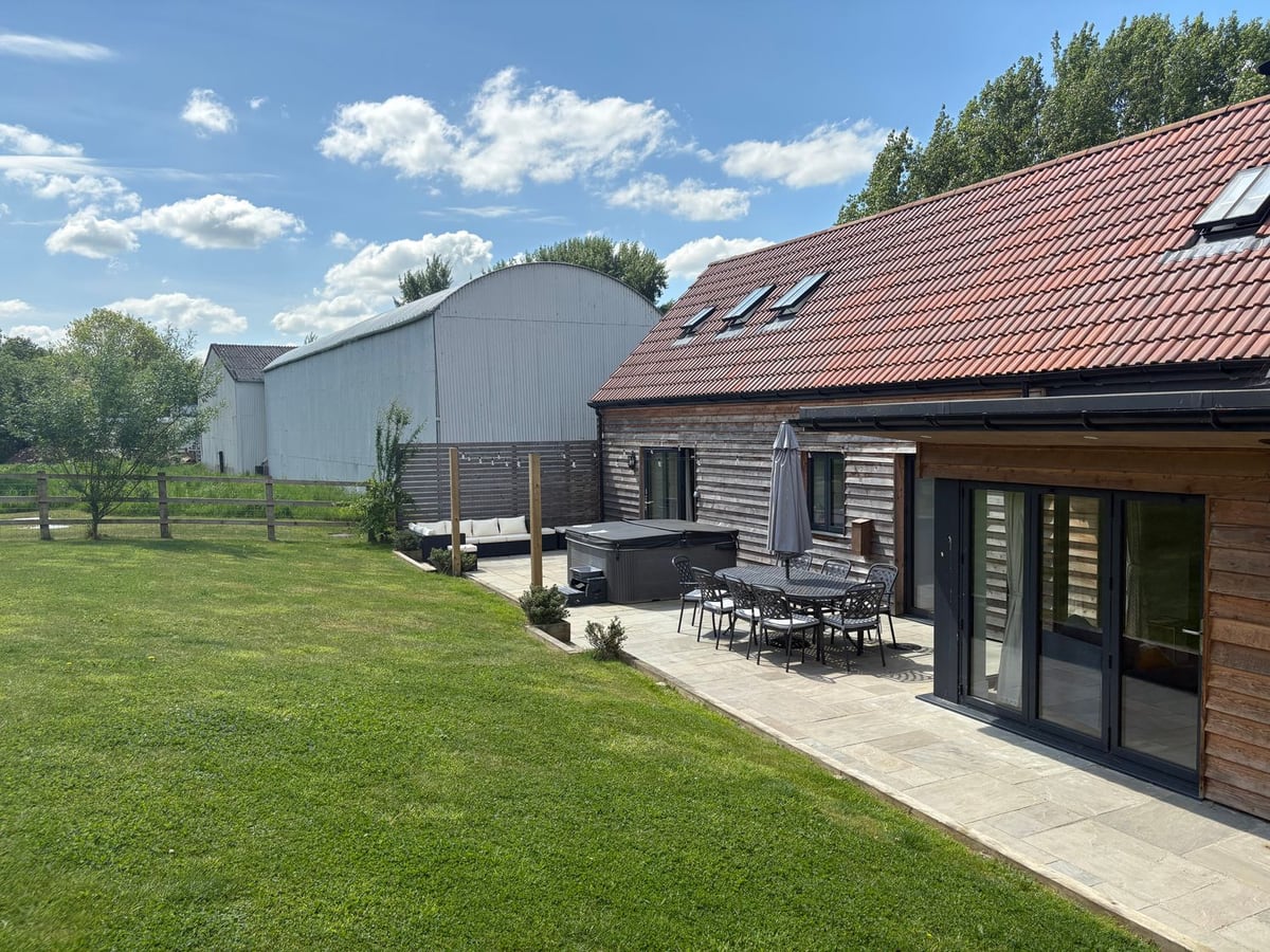 Lawn beside the timber-clad Gully, with a covered hot tub, patio table and open folding doors